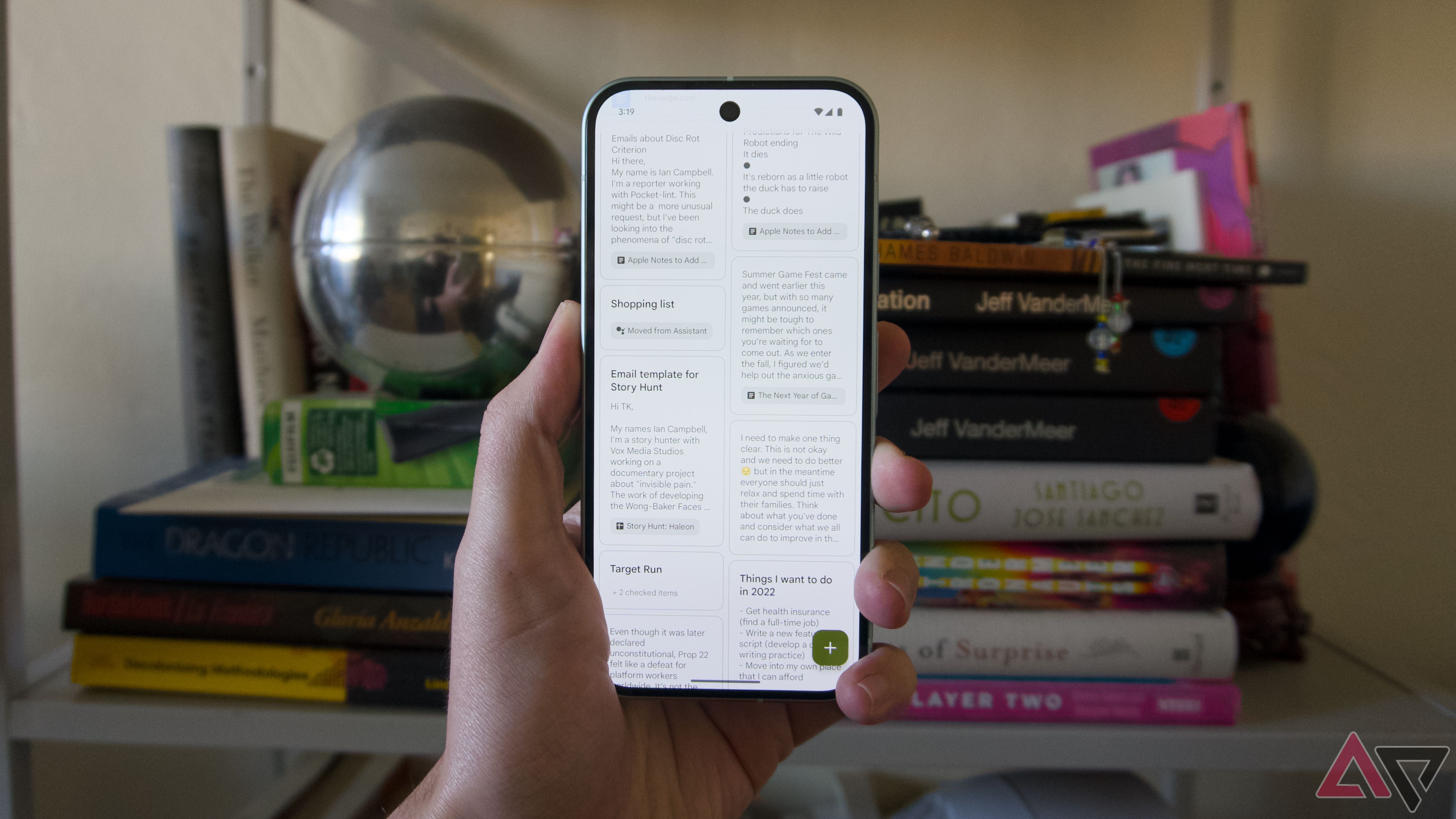 A hand holding a Pixel 9 running Google Keep in front of a bookcase. 