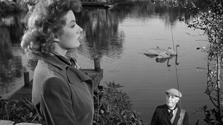 Greer Garson as Kay Miniver looks into the distance while Henry Travers as Mr. Ballard watches her in front of a lake in Mrs. Miniver