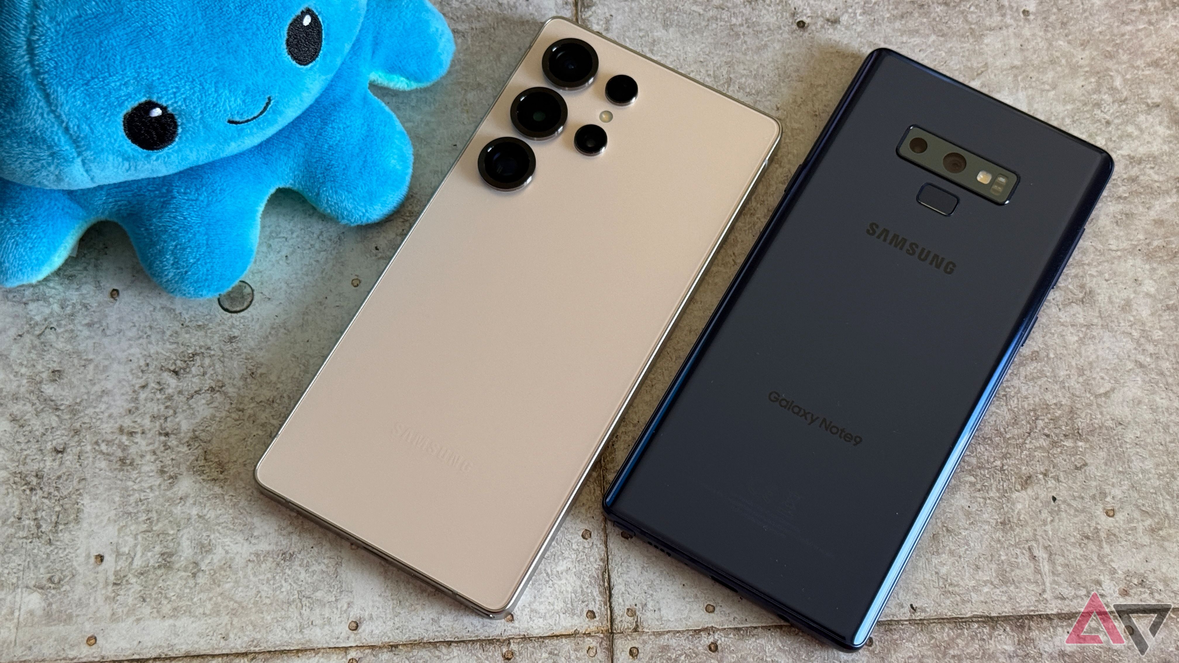 A Samsung Galaxy Note 9 and Galaxy S25 Ultra side by side on a tile flor with a blue plushie