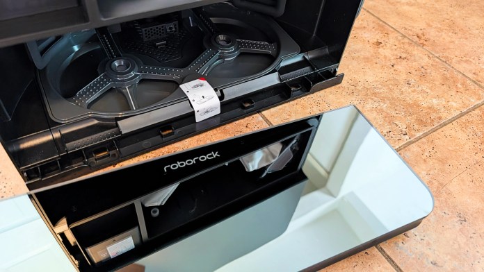 An open Roborock vacuum dock showing the internal compartments and a mirrored surface.