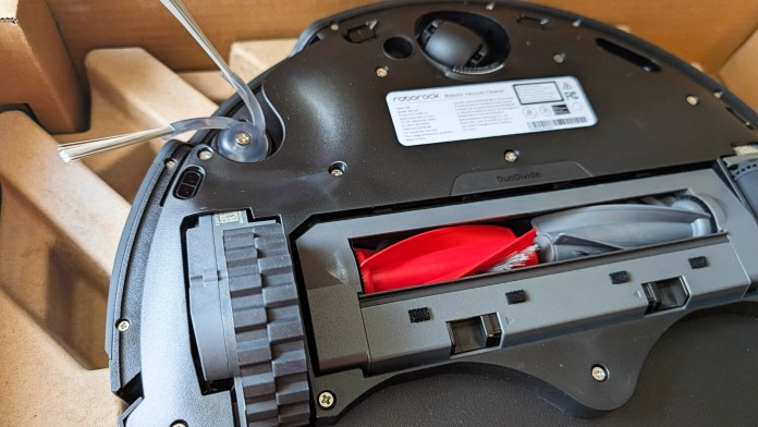 Close-up view of the underside of a Roborock Saros 10R robot vacuum cleaner, featuring the DuoDivide anti-tangle brush system and compartment for additional cleaning tools.