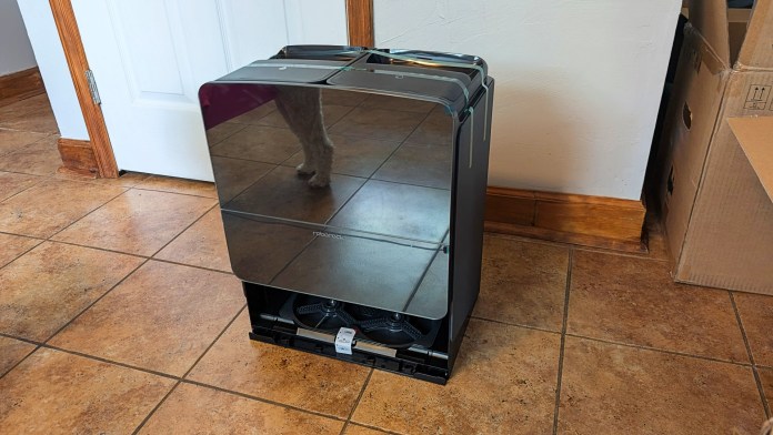A Roborock Saros 10R robot vacuum and mop dock with a sleek mirrored surface, positioned on a tiled floor near a door.
