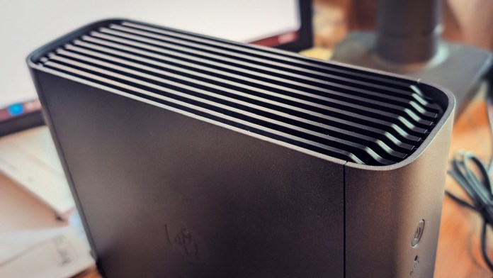 A close-up view of the Synology BeeStation Plus, featuring a sleek black design with horizontal slits for ventilation, positioned on a wooden desk with a blurred background.