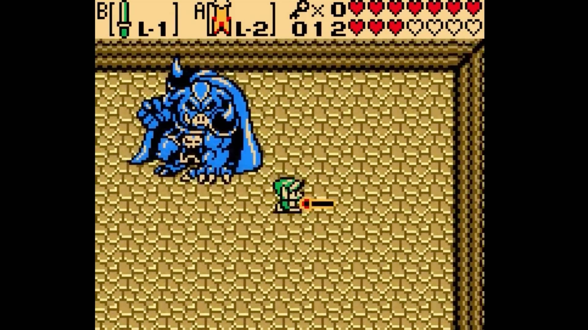 A pixelated video game scene shows a small character in green facing a large blue creature on a patterned floor