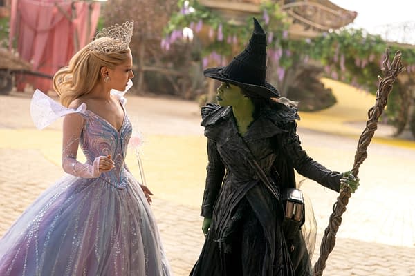 A promotional still from 'WICKED FOR GOOD' featuring Ariana Grande as Glinda in a sparkling gown and Cynthia Erivo as Elphaba, dressed in a black cloak and pointed hat. The scene captures a tense interaction between the two characters within a colorful, fantastical setting.