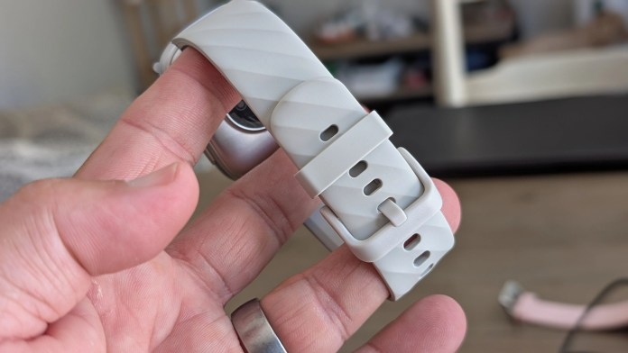 Close-up of a hand holding a light gray smartwatch band with a textured design and adjustable buckle.
