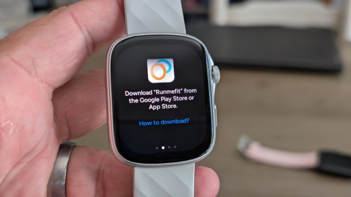 Close-up of a smartwatch displaying a message to download the Runmefit app from the Google Play Store or App Store, held in a person's hand.