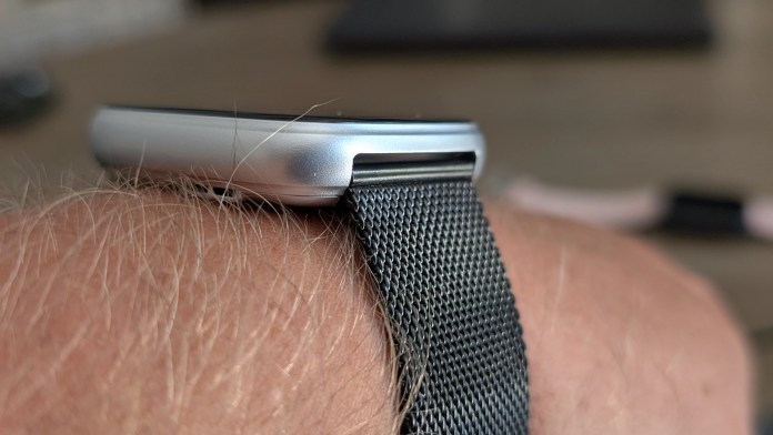 Close-up view of a smartwatch with a silver frame and a black mesh band worn on a wrist.
