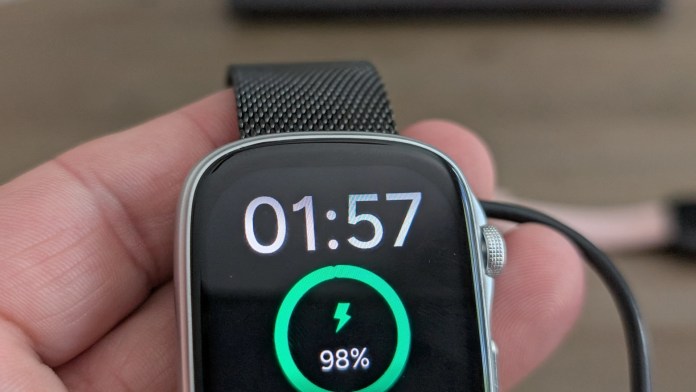 Close-up of a smartwatch display showing a charging indicator at 98% battery and the current time as 01:57.