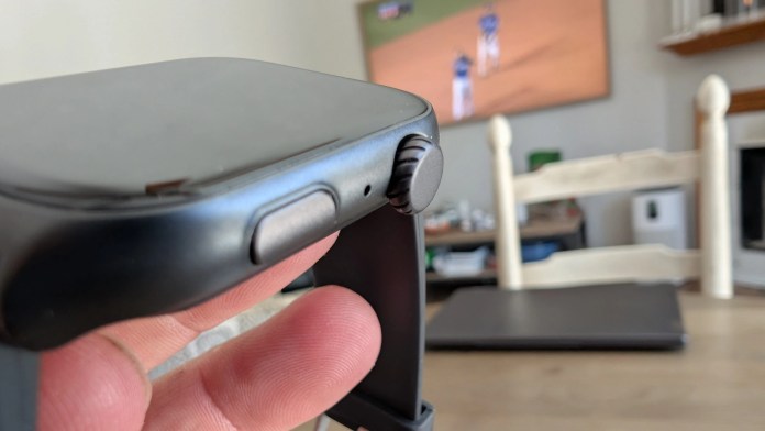 Close-up view of the Runmefit Watch 4 smartwatch showcasing its side buttons and screen, with a blurred background featuring a living room setting.