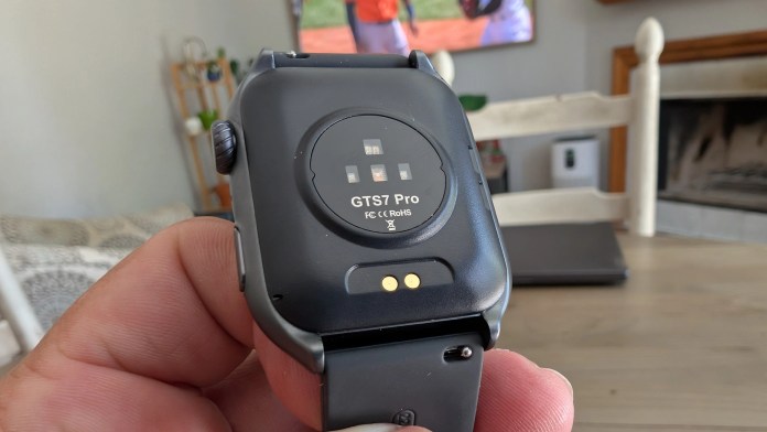 Close-up view of the Runmefit GTS 7 Pro smartwatch from the back, showing the charging contacts and model details, held in a person's hand.