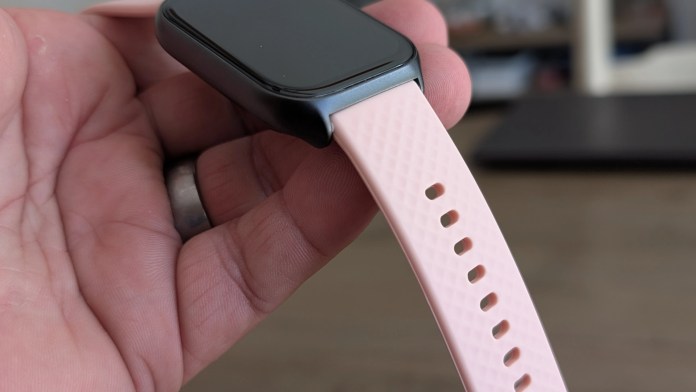 Close-up view of the Runmefit Watch 4 being held in a hand, showcasing its sleek design and pink silicone strap.