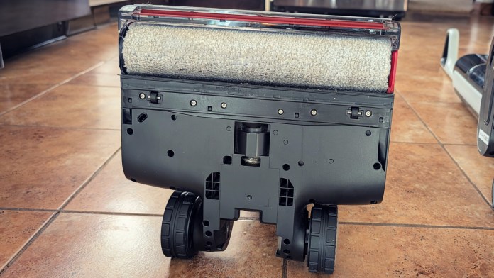 Close-up view of the underside of a wet/dry vacuum cleaner with a roller brush and wheels, resting on a tiled floor.