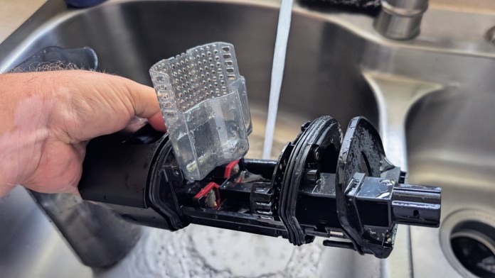 A person holding a vacuum cleaner component under running water in a kitchen sink, demonstrating the cleaning process.