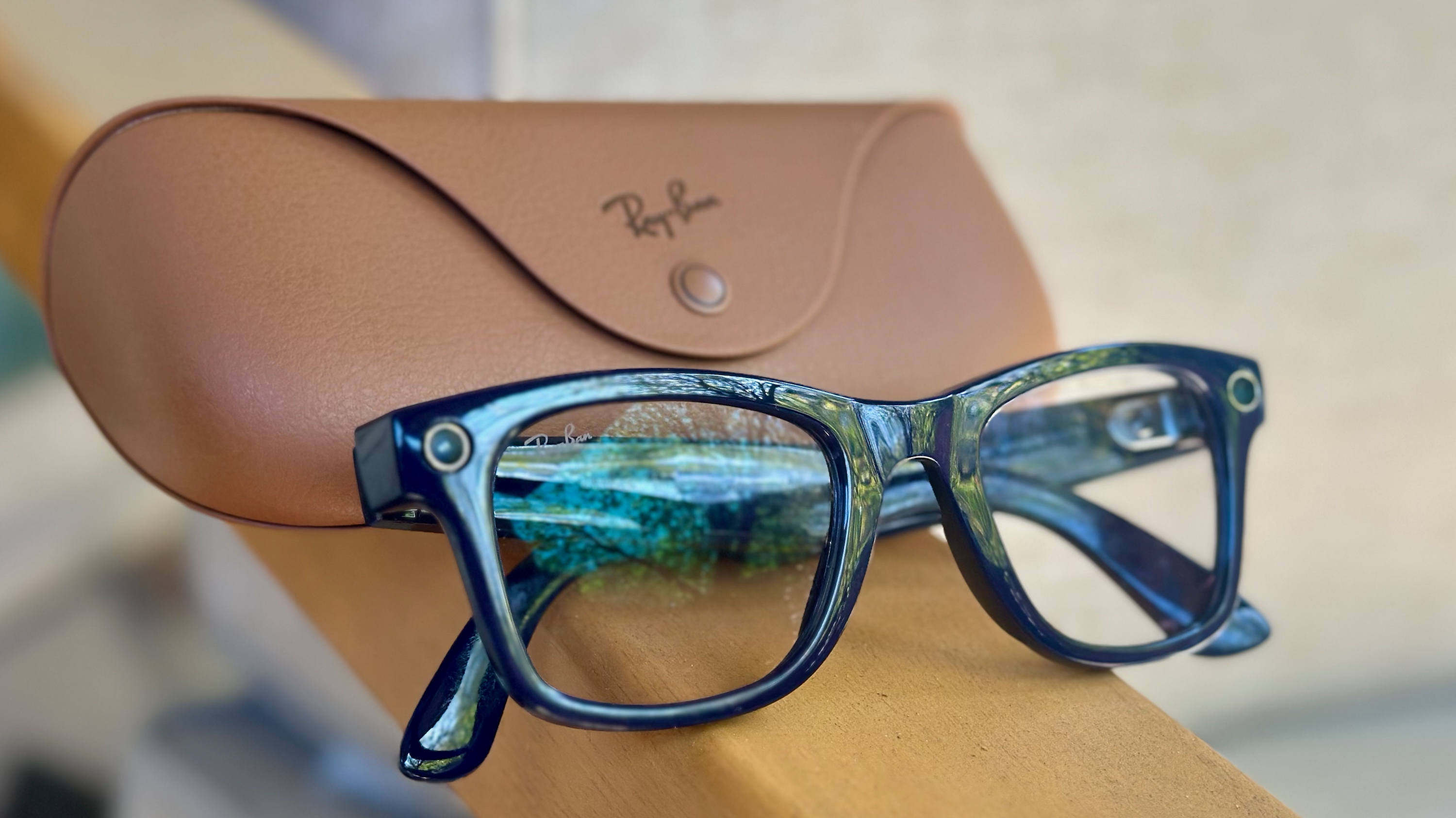 Close-up photo of the Shiny Cosmic Blue Ray-Ban Meta (Gen 2) Wayfarer glasses sitting folded up on an armrest with the official brown Ray-Ban charging case behind it.