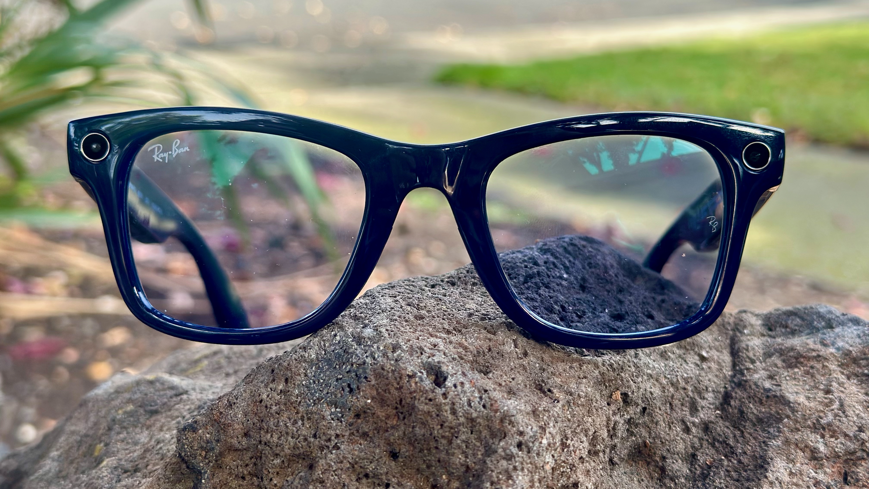 A photo of the Ray-Ban Meta (Gen 2) smart glasses sitting on a rock, close up of the front lenses and camera cutouts.
